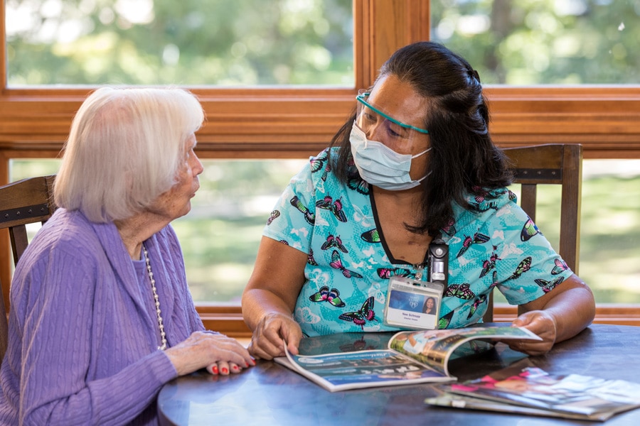 Employee In Mask Discussing Magazine With Resident