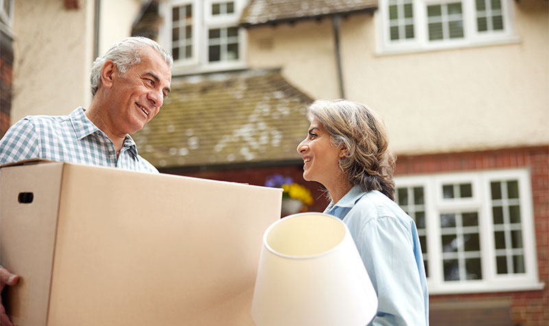 Elderly Couple Outside Home Holding Boxes