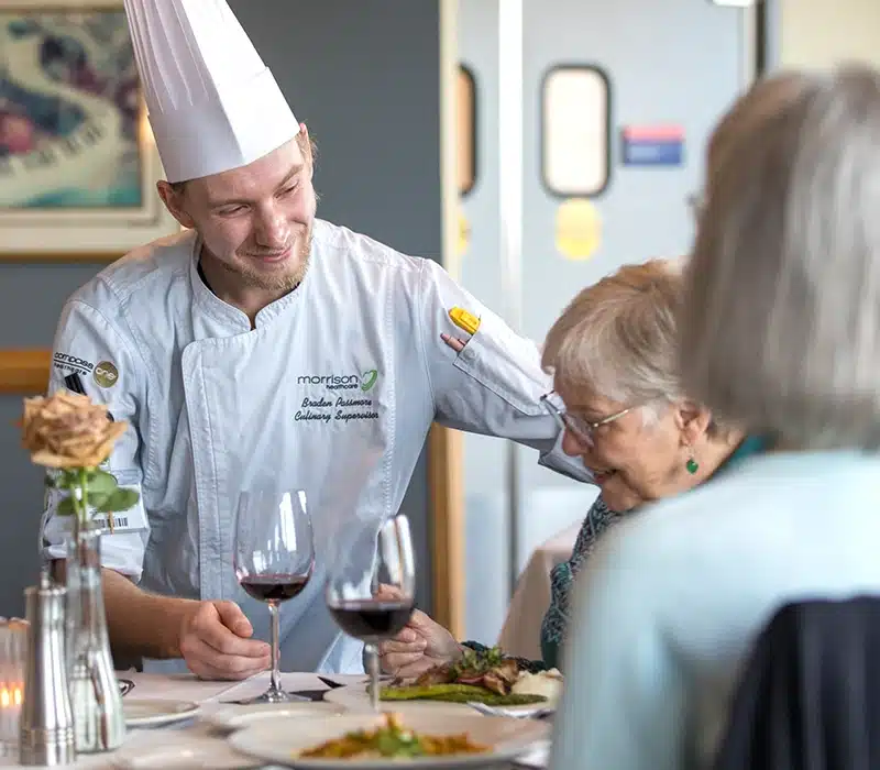 Chef Standing By Dining Table With Residents